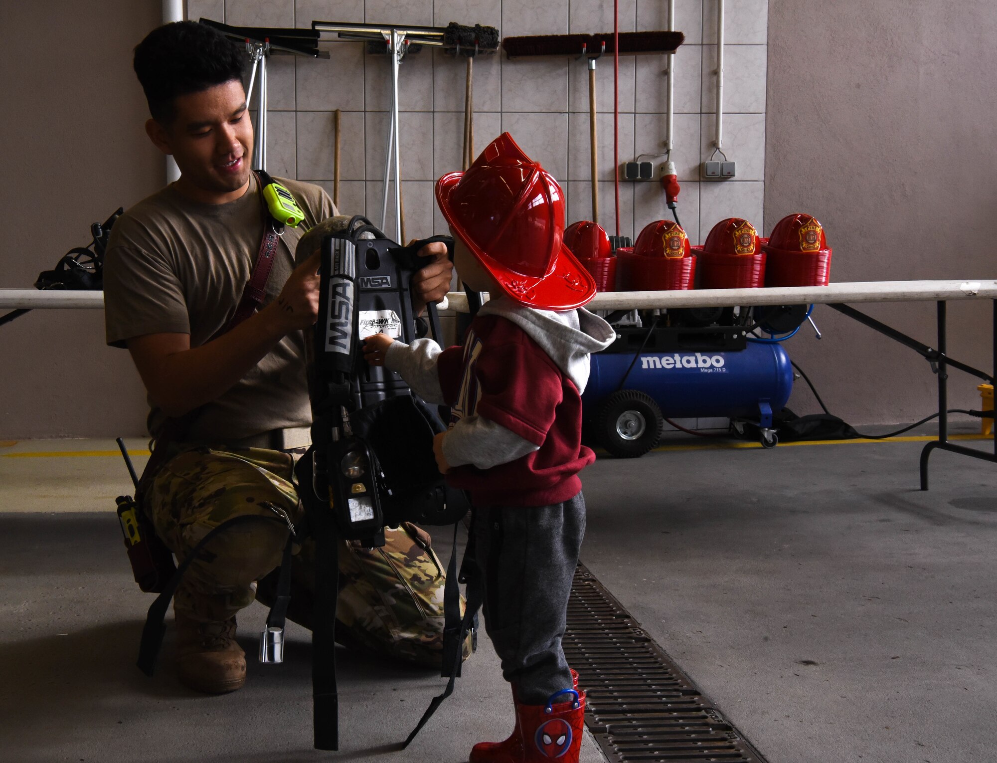 U.S. Air Force Airman 1st Class Mason R. Kim, 86th Civil Engineer Squadron fire department fire fighter, helps a child into firefighting gear during a Fire Prevention Week