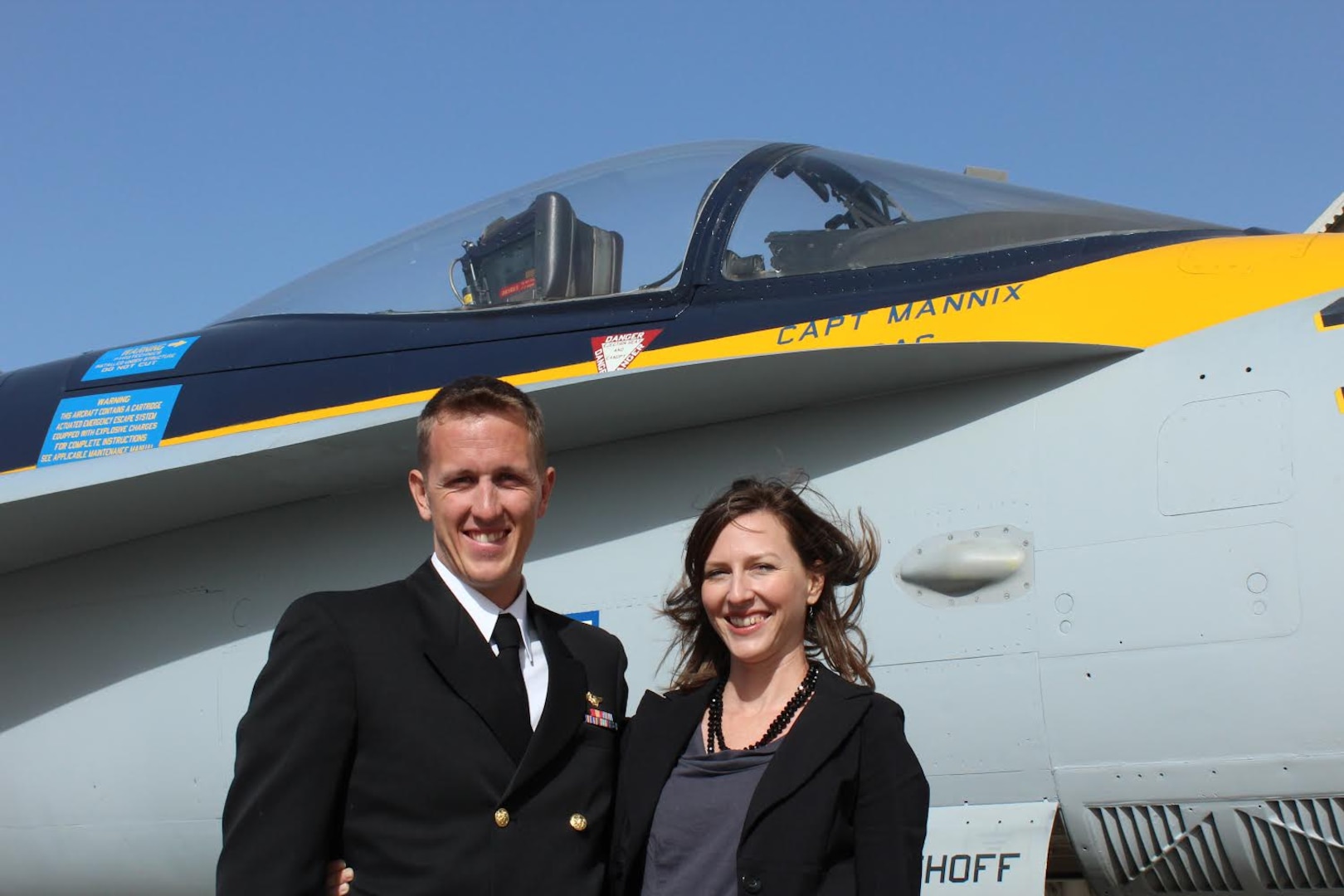 Man in uniform and woman in suit pose in front of an aircraft