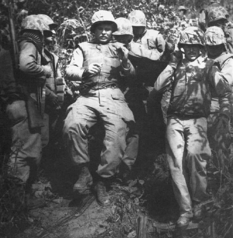 Men move down a hill, some of whom are carrying a litter.