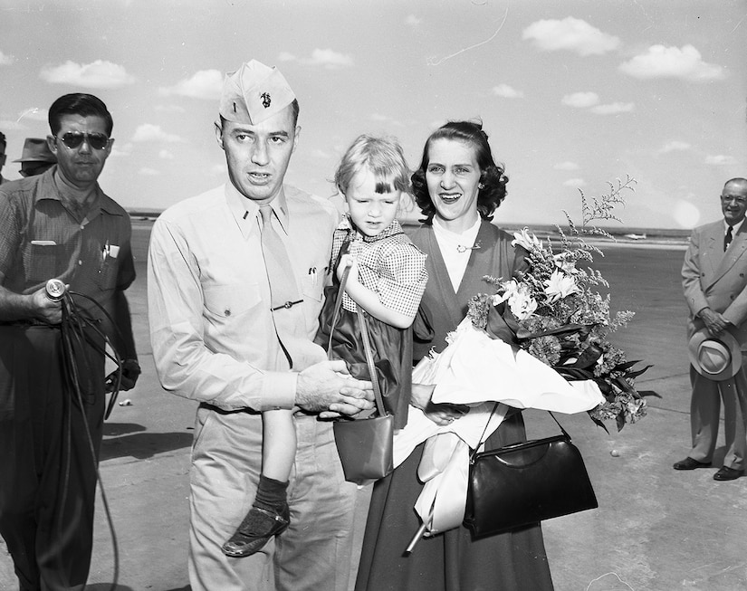 A man carries a small child in his arms as a woman carrying flowers walks beside him.