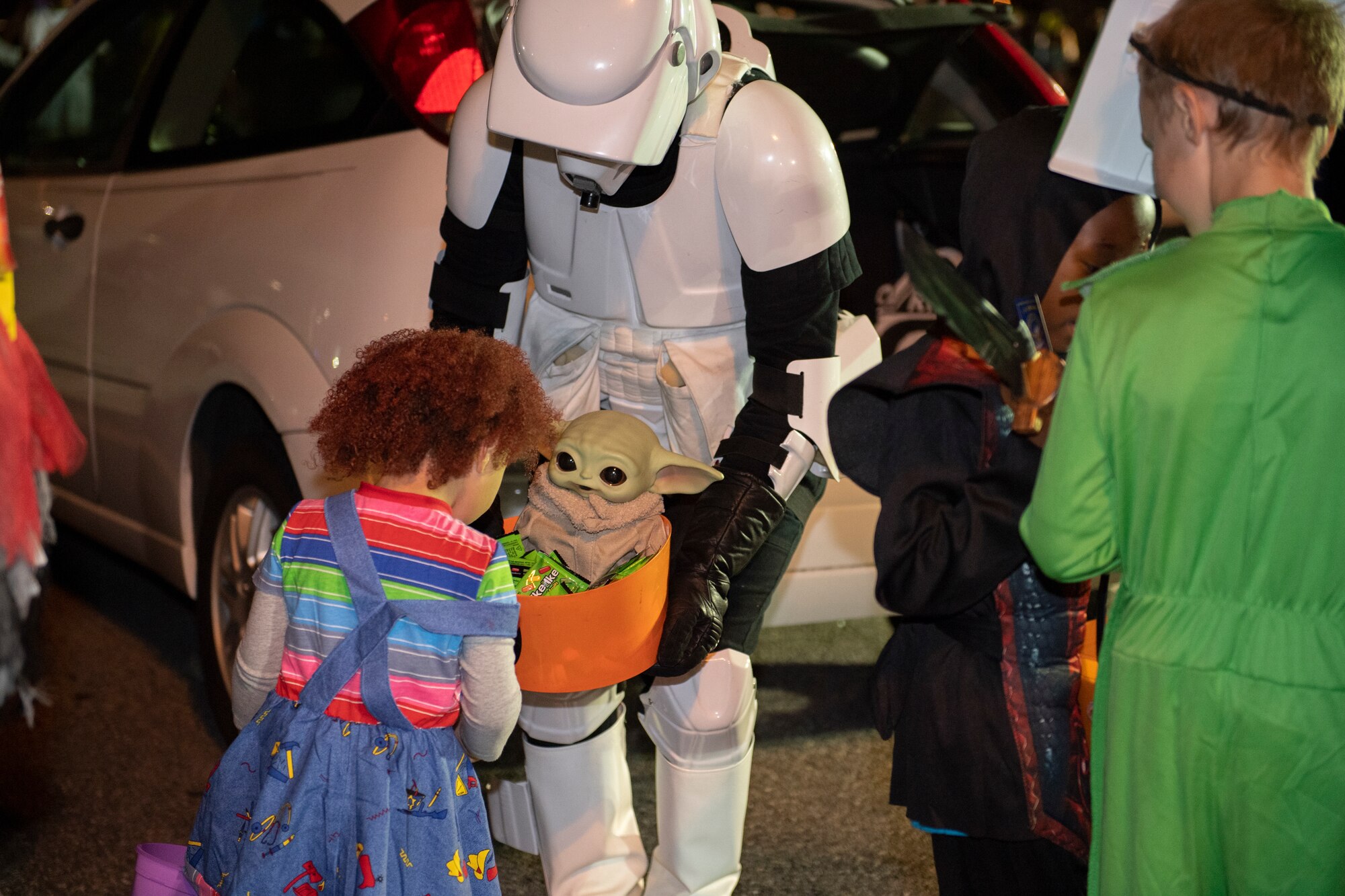 A photo of a man wearing a costume passing candy out to a child wearing a chucky costume.