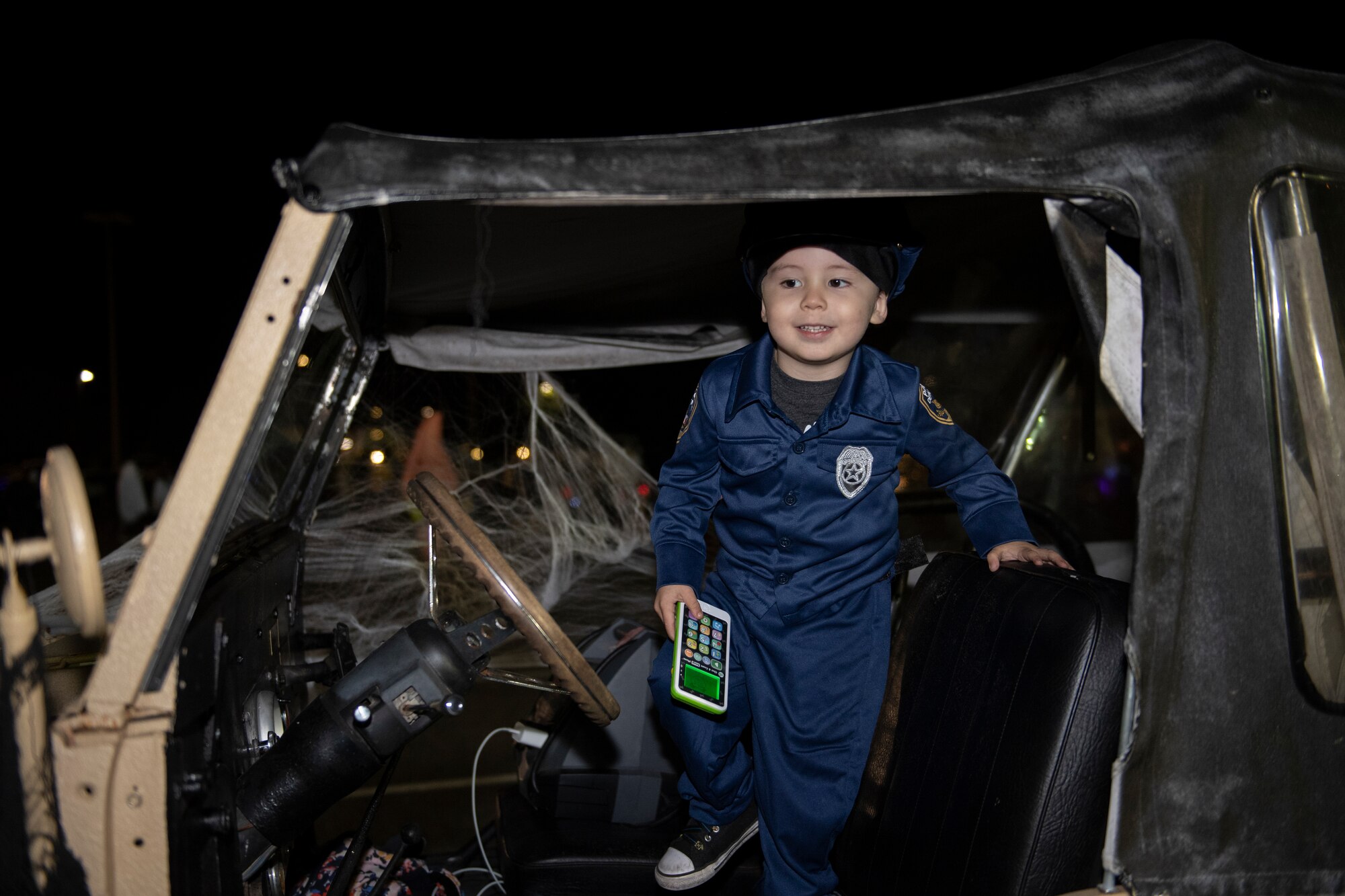 A photo of a young boy dressed in a cop costume standing in the drivers side of a jeep.