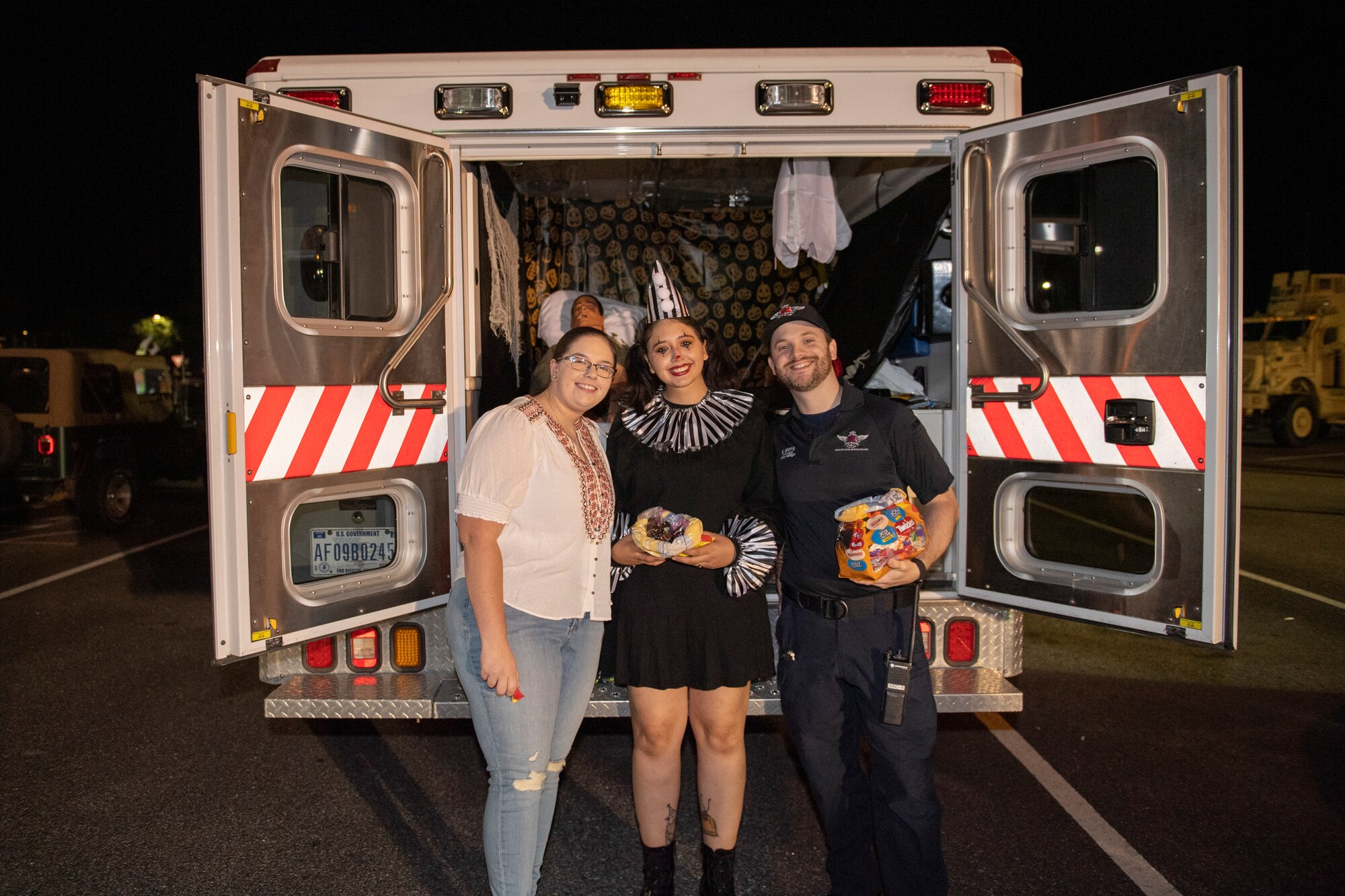 A photo of three people dressed in halloween costumes standing at the back of an ambulance posing for a photo.