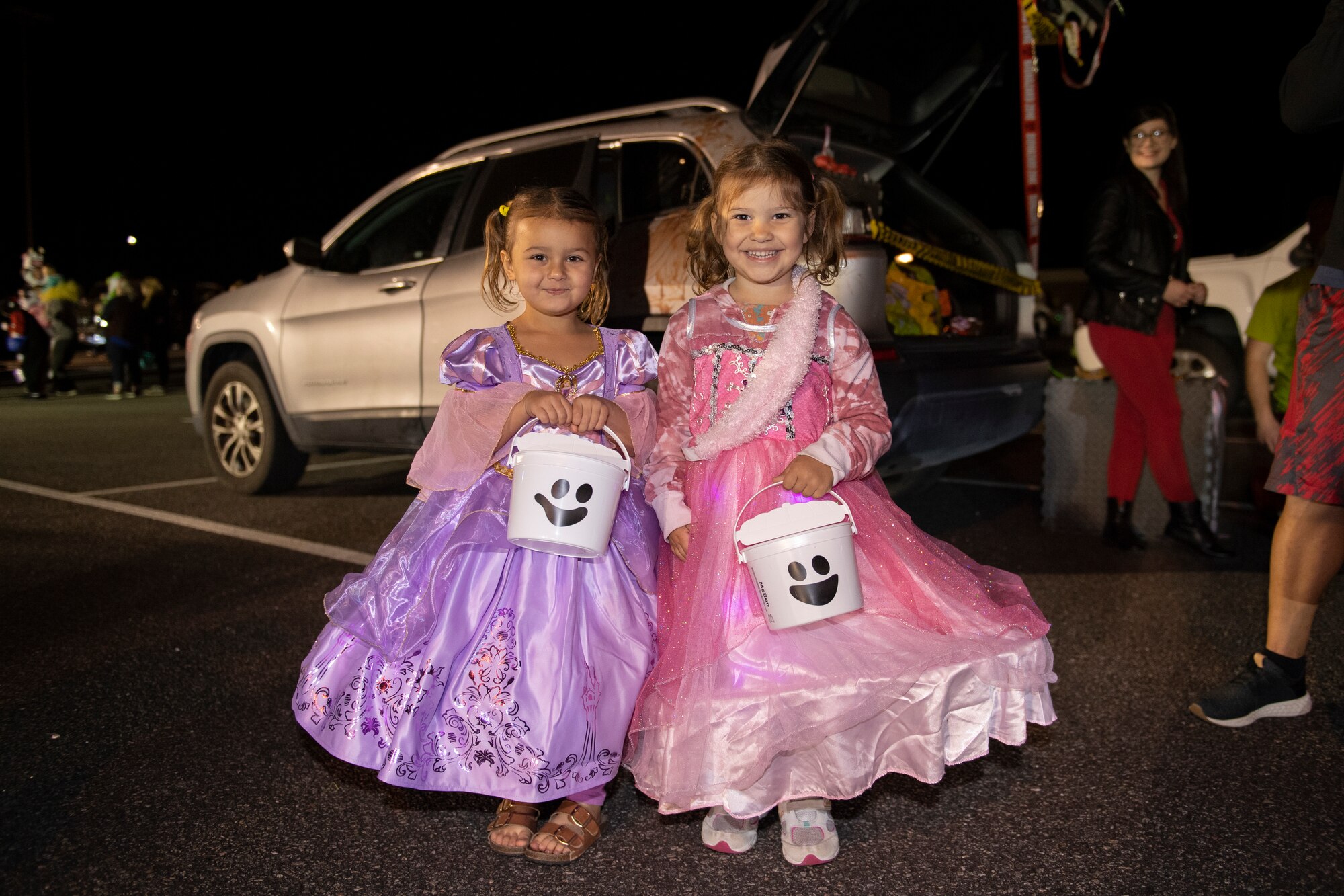 A photo of two young girls wearing princess dresses holding white Halloween buckets with smile faces on them.