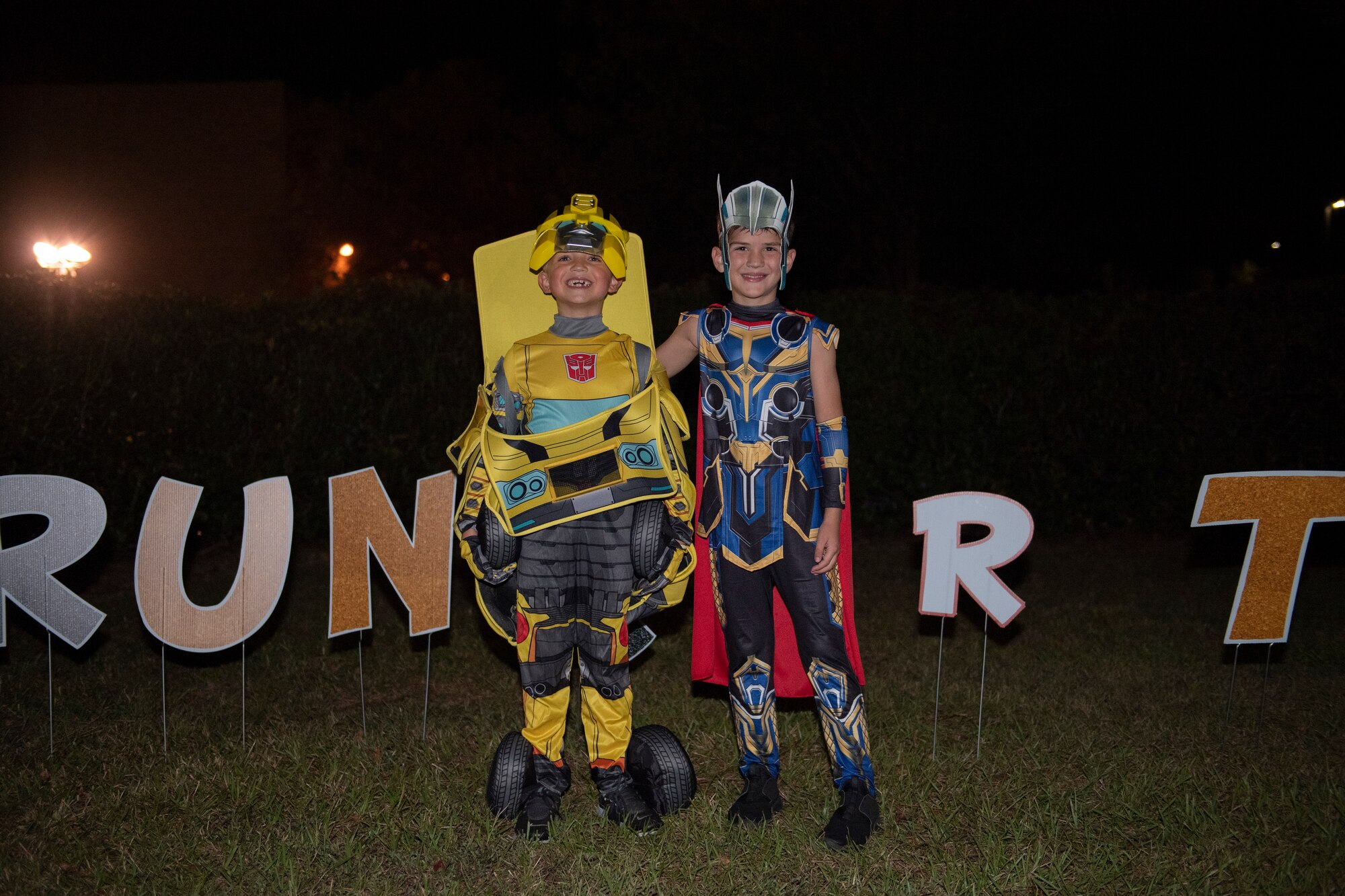 A photo of two kids standing in front of a Trunk or Treat yard sign.