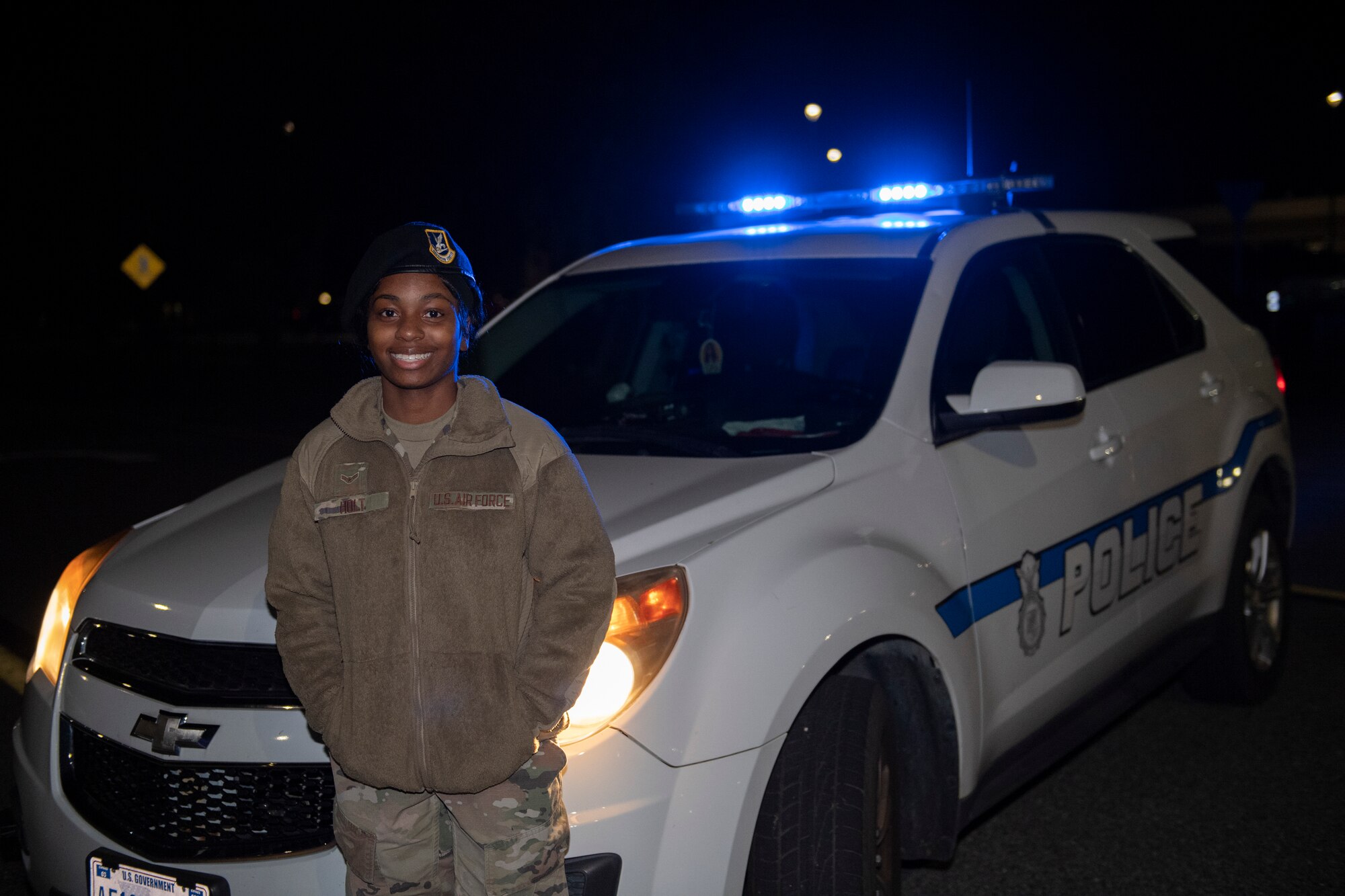 A phot of a woman cop standing at the front of her patrol car, posing for a photo.