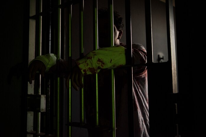 Beale volunteer Airman hangs his arms through prison bars at the haunted house at Beale Air Force Base