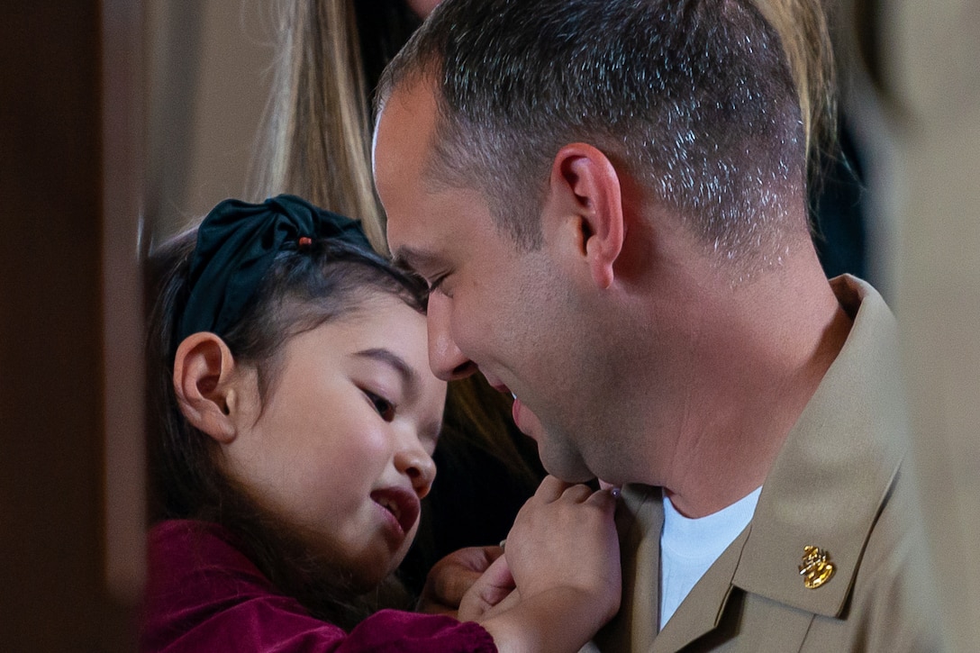 A child pins an anchor onto the lapel of a sailor's uniform.