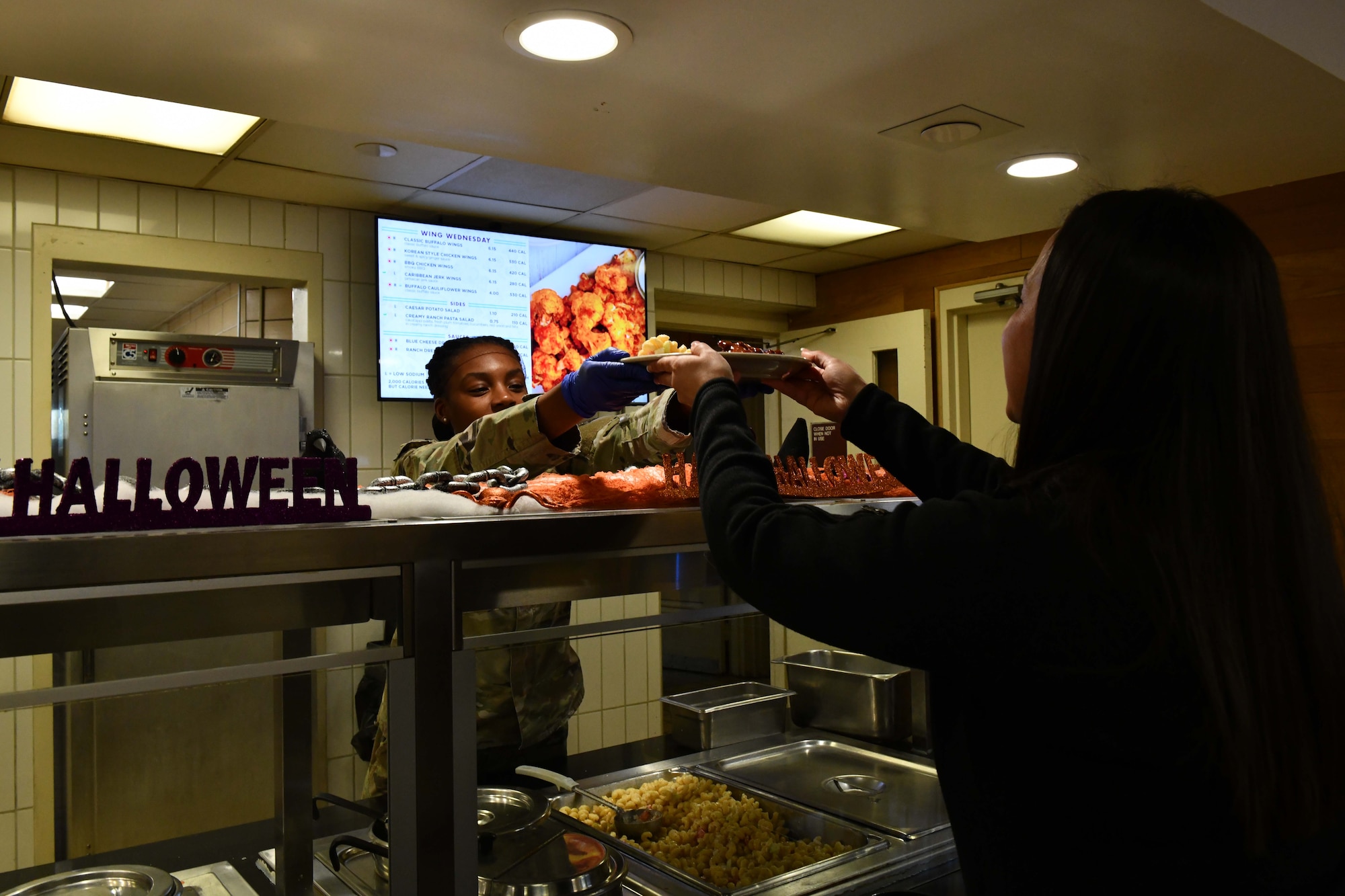 U.S. Air Force Airman Kimbrea Sparks, 97th Force Support Squadron food services apprentice, gives a plate to Tech. Sgt. Ariel Almquist, 54th Air Refueling Squadron aviation resource management noncommissioned officer in charge, at Altus Air Force Base, Oklahoma, Oct. 19, 2022. Hangar 97, Altus’s dining facility, offers a wide array of meal choices with a menu that changes quarterly. (U.S. Air Force photo by Airman 1st Class Miyah Gray)