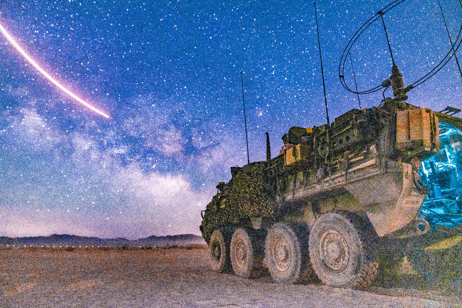 A military vehicle sits on a field underneath a starry sky.