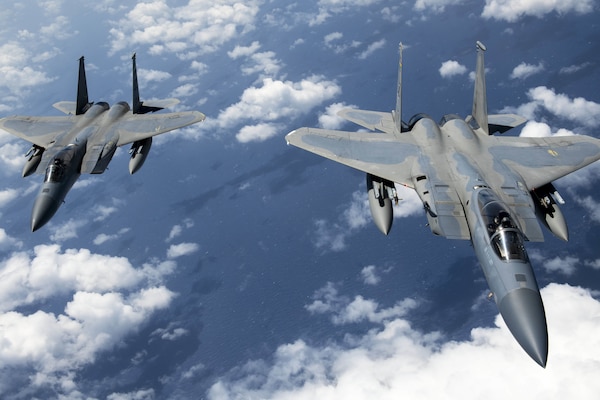 Two military aircraft fly over a blue sea and clouds.