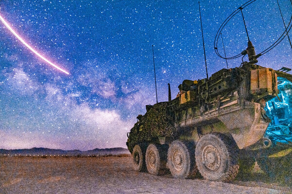 A military vehicle sits on a field underneath a starry sky.