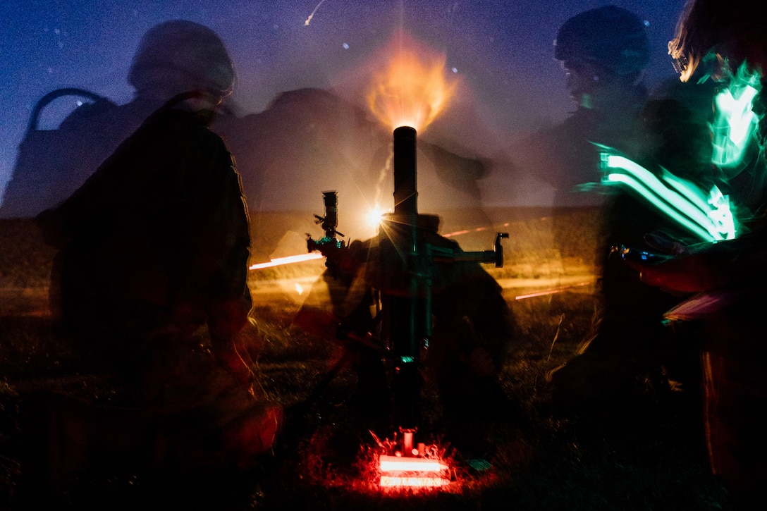 Soldiers fire a mortar system at night.