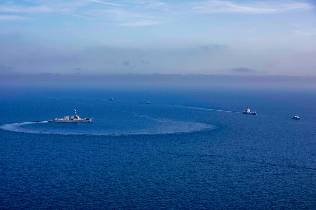 A group of ships sail in formation in the ocean.