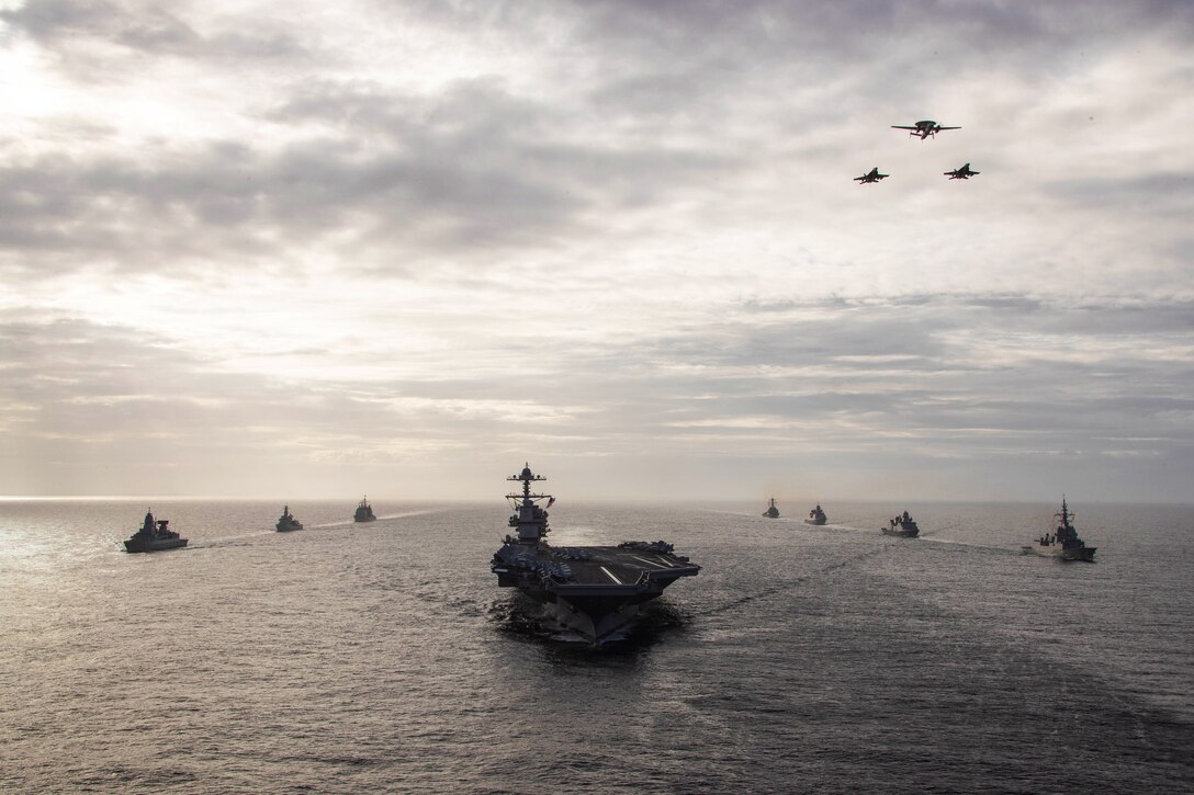 Aircraft fly over ships as they sail in formation.