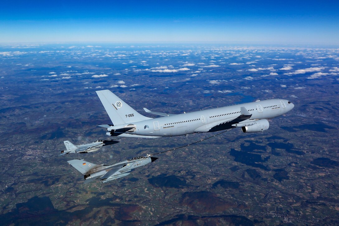 A large aircraft is refueled by smaller aircraft in midair.