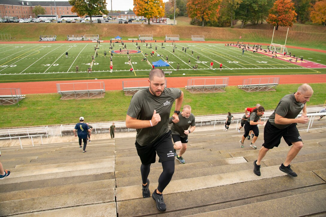 Some participants run up the stadium stairs while others perform other activities on the field below.