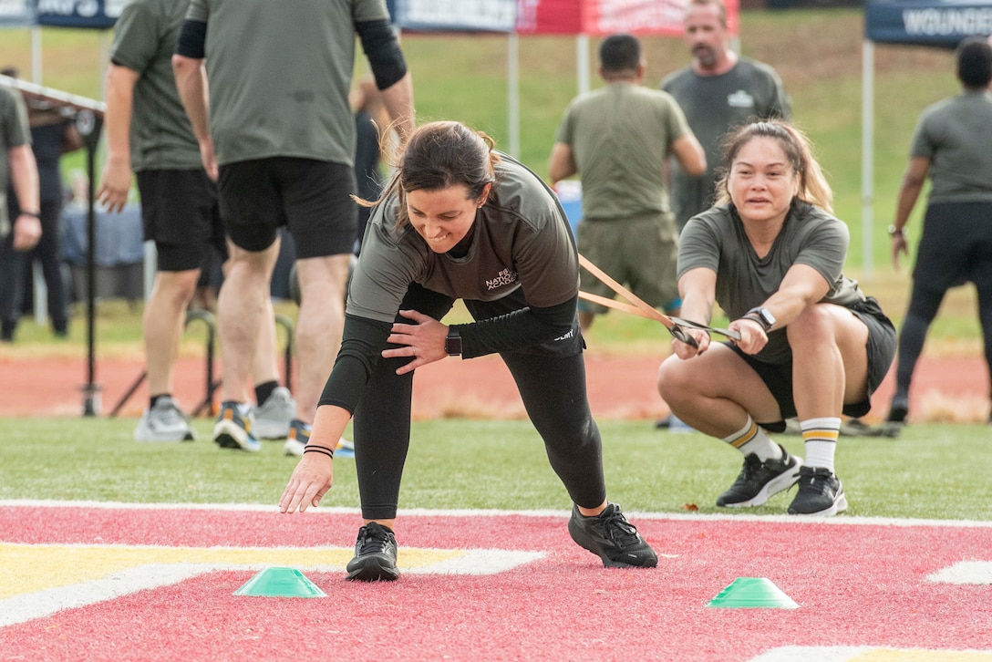 A participant tries to reach forward to touch a cone while being held back by a partner using exercise bands.