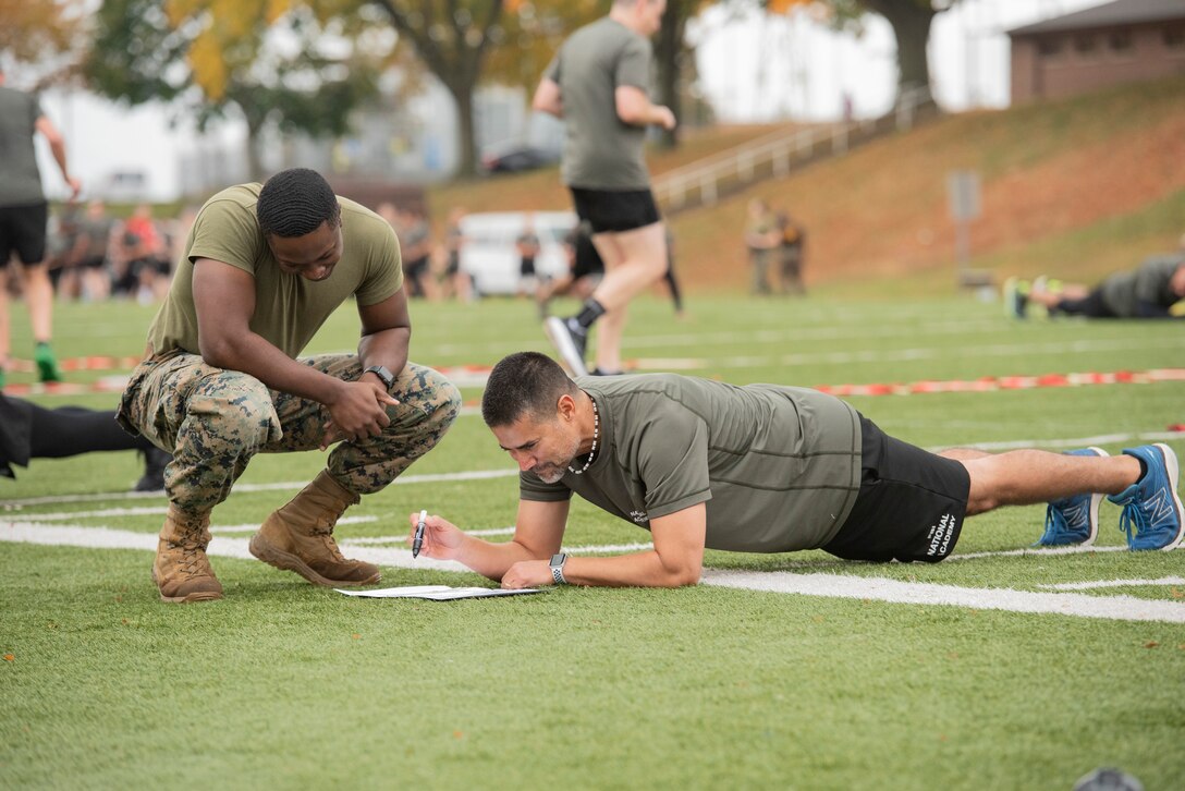 A Marine watches a participant plank while solving a cognitive puzzle.