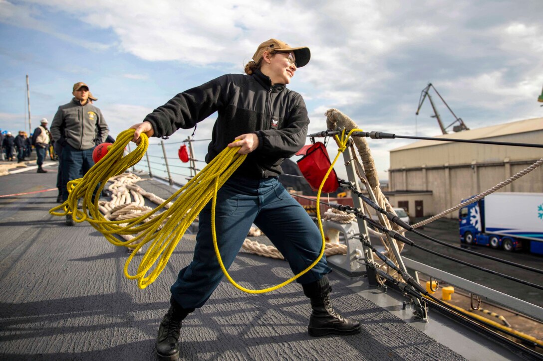 A sailor throws a yellow rope off a ship to a pier.