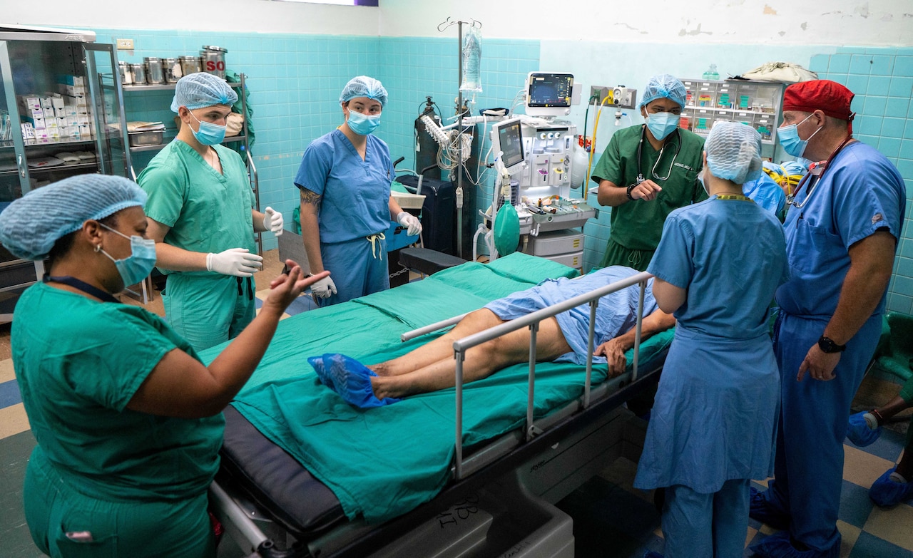 Personnel in surgical gowns surround a patient on a hospital bed.