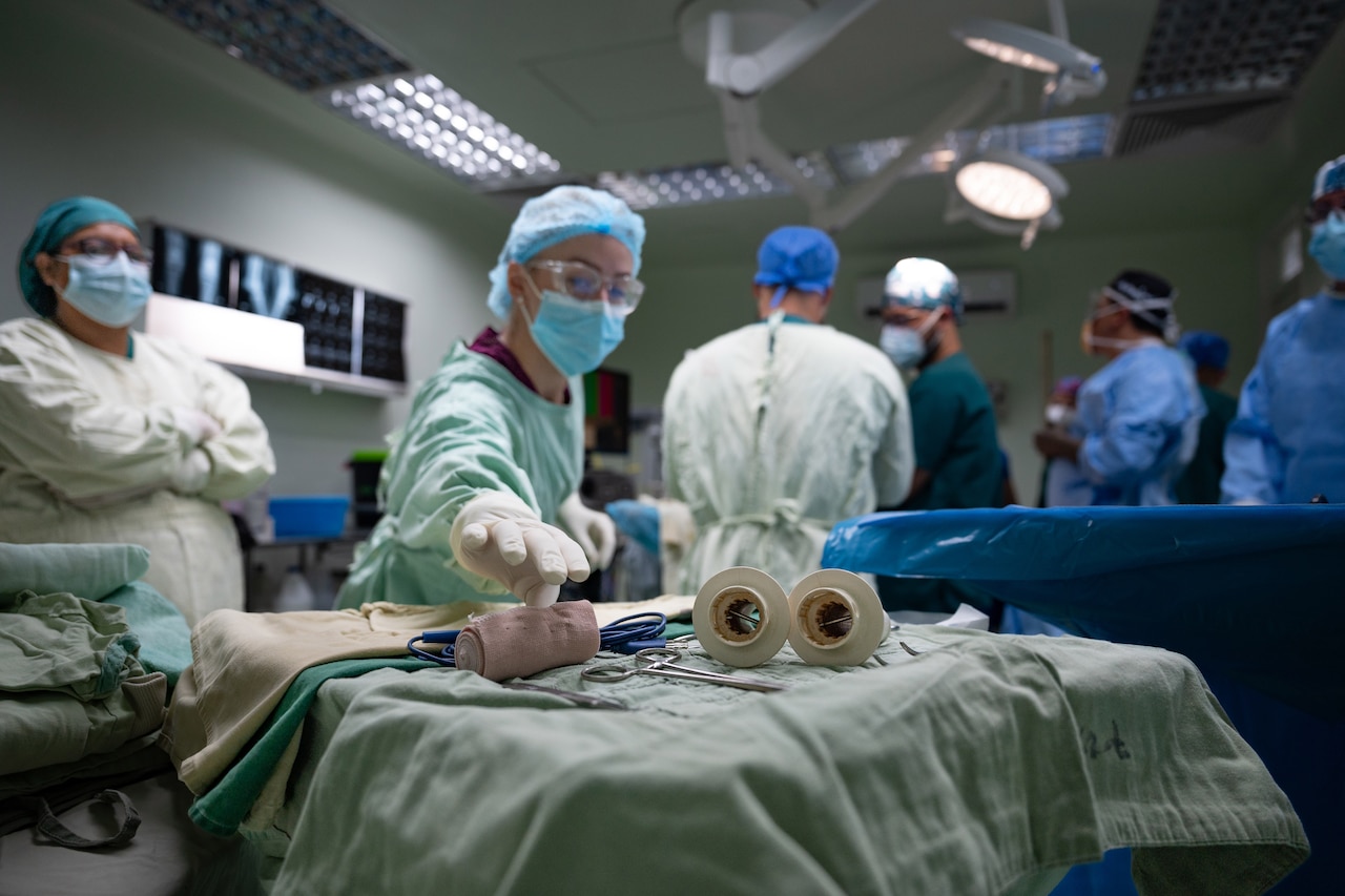 A medical professional reaches for medical equipment.