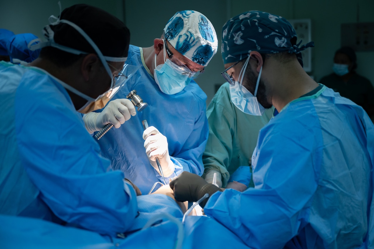 Three medical professionals work on a patient during surgery.