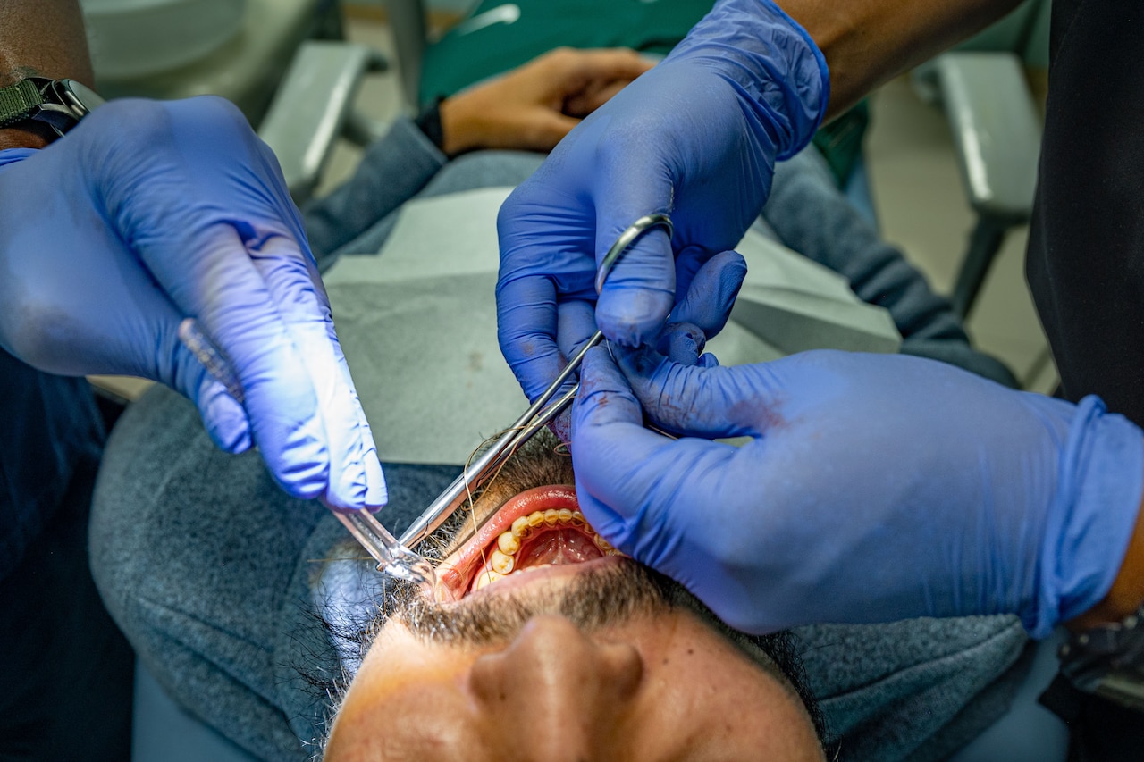 Dental professionals put stiches into the mouth of a patient.