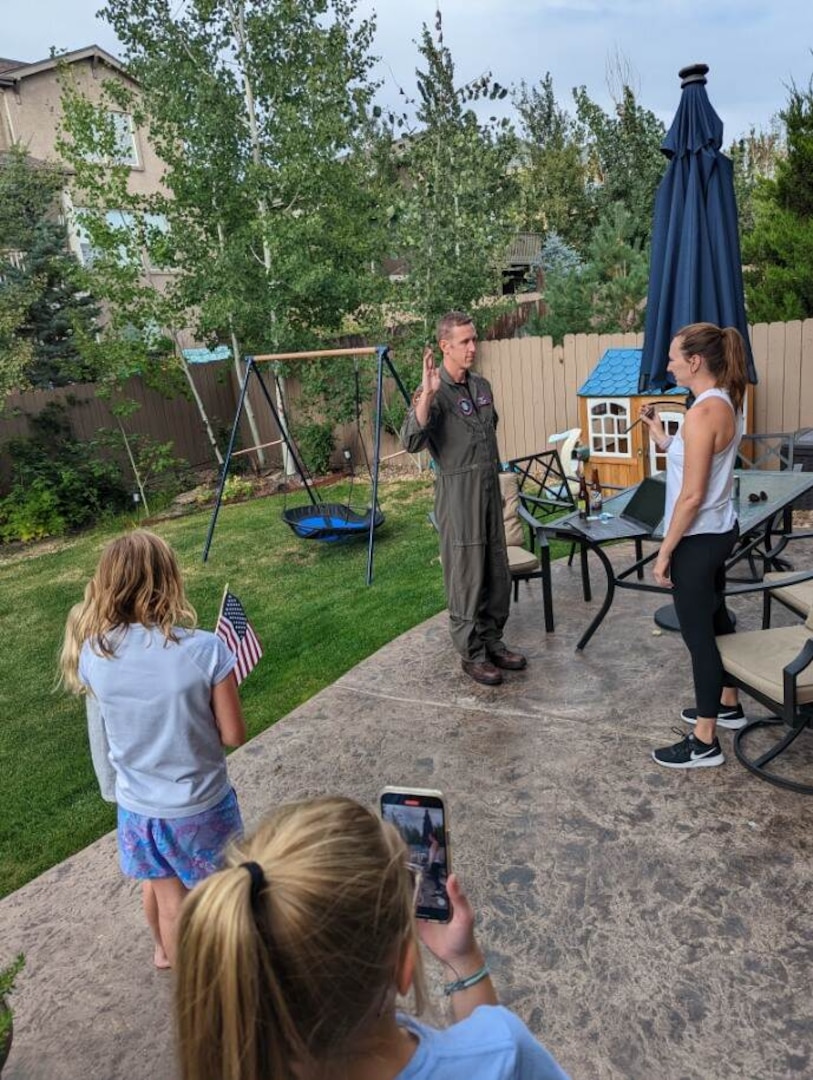 Man in uniform lifts his right hand to take the oath of office in front of his wife and two daughters