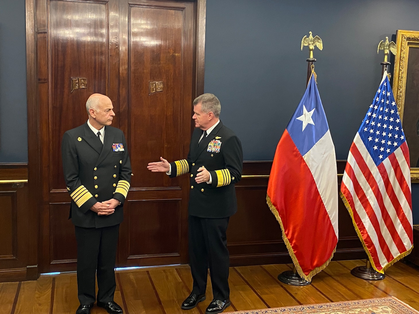 Adm. Samuel Paparo speaks with Adm. Juan Andres De la Maza next to the flags of Chile and the United States.