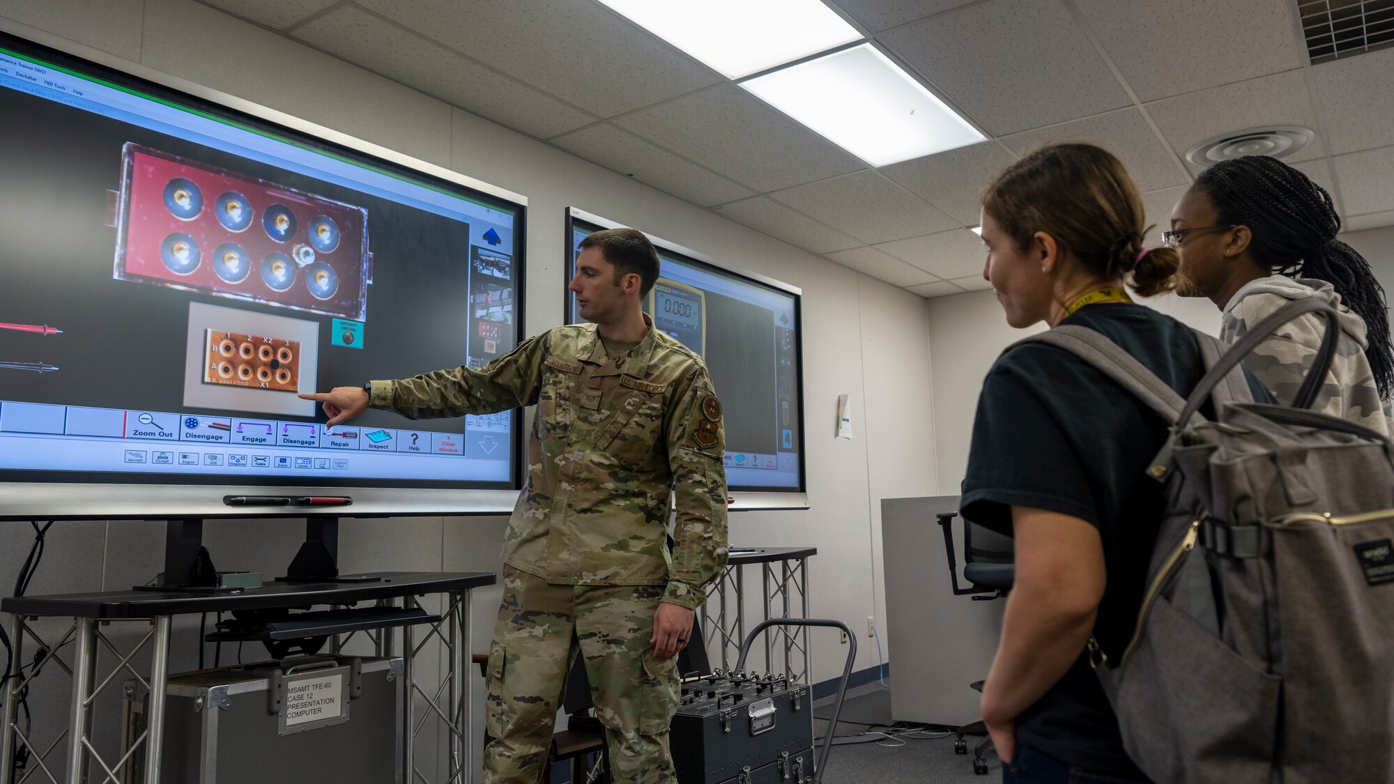 Instructor points at an interactive screen with components of a fighter jets on it.