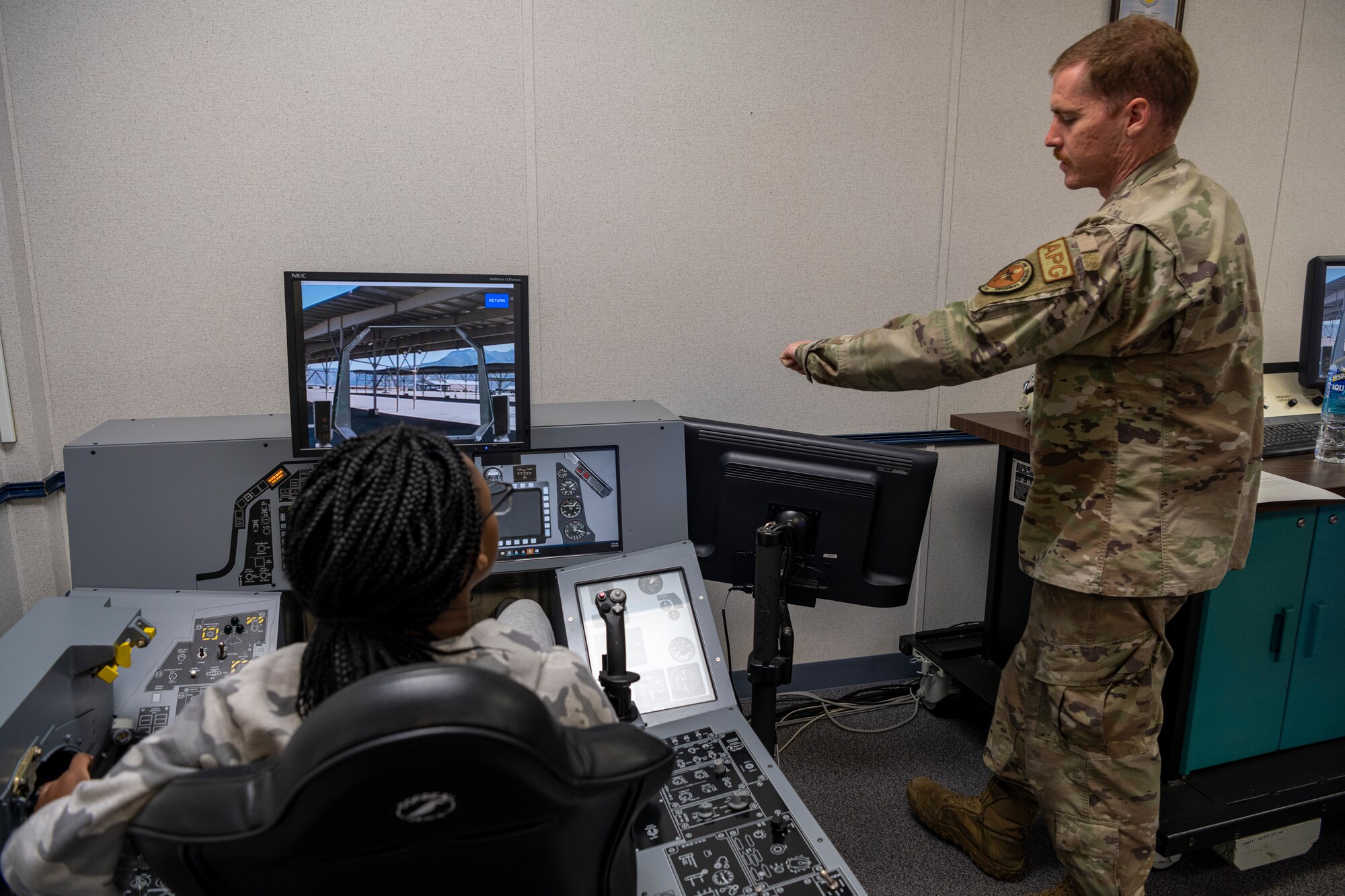 Airman showing student how to increase the throttle on a fighter jet in a simulator.
