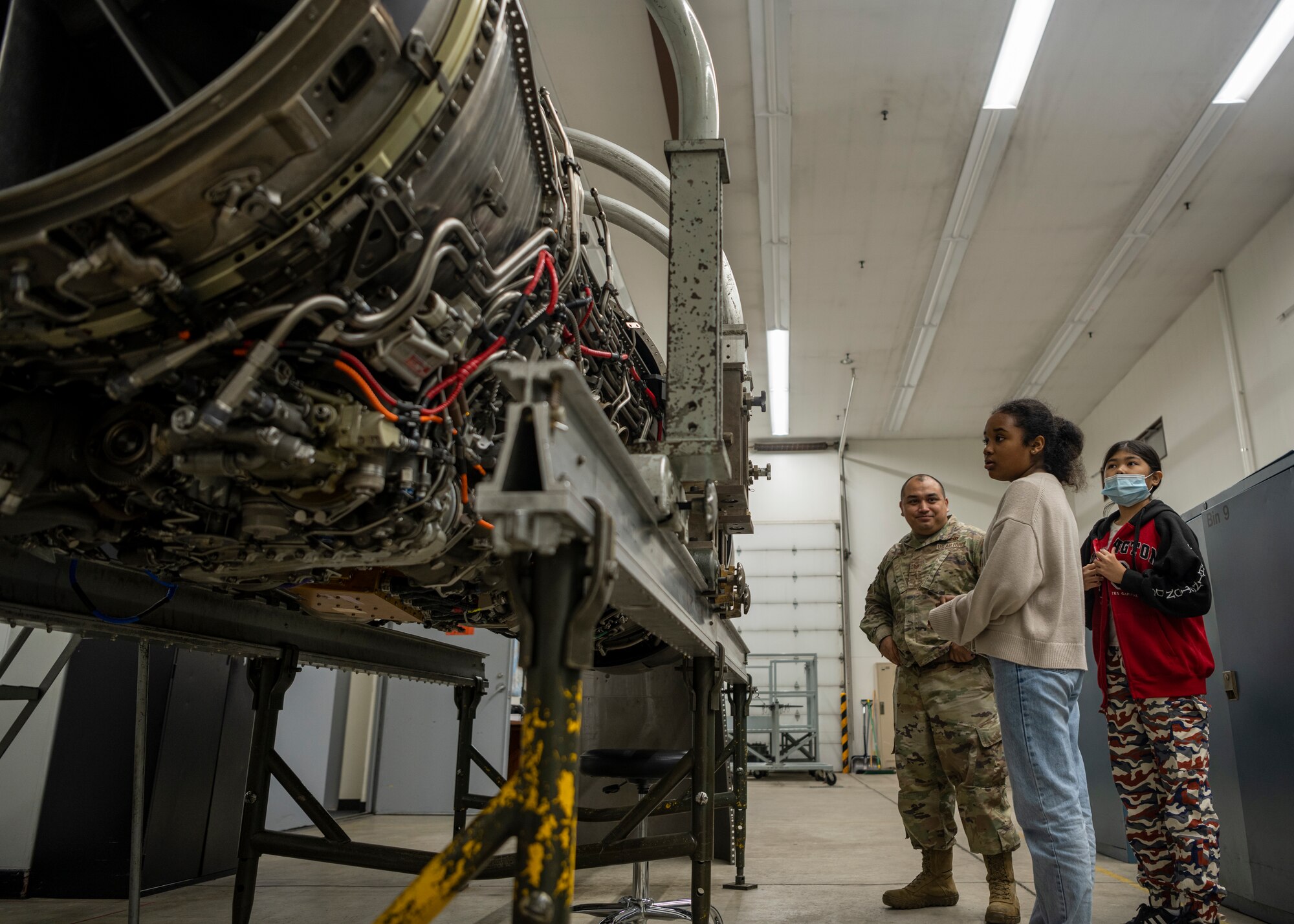 Students stand in front of a huge fighter jet engine during a tour.