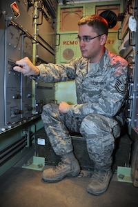 Man in camo uniform touches a knob on a control panel in a trailer.