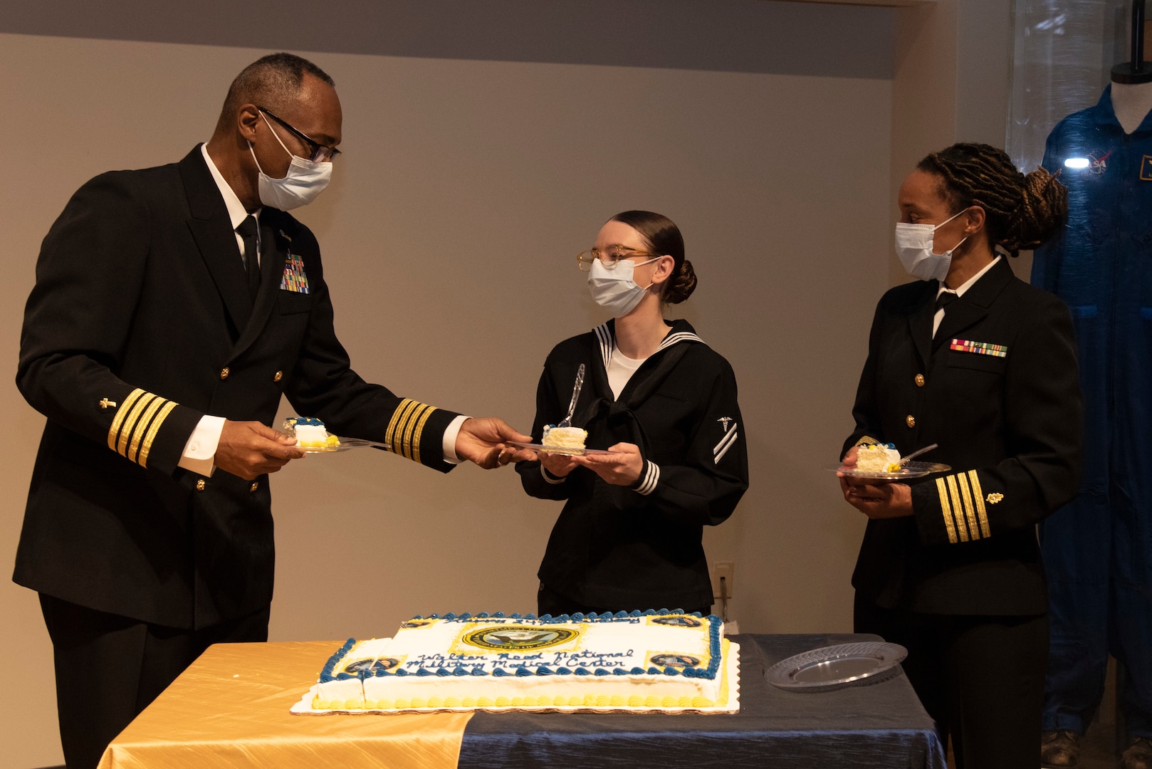 Capt. Herbert Griffin, left, chief of pastoral care at Walter Reed National Military Medical Center (WRNMMC), passes a slice of cake to Hospital Corpsman Apprentice Paige Zimmer-Duncan, center, assigned to WRNMMC, during a U.S. Navy 247th Birthday Ceremony in Memorial Auditorium at WRNMMC in Bethesda, Maryland, Oct. 13, 2022. Navy Medicine Readiness and Training Command, Bethesda, hosted the ceremony with Capt. Kelly Elmore, WRNMMCs chief of staff, as the guest speaker.