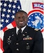 Soldier standing in dress uniform in front of the American flag.