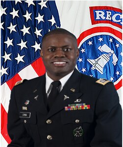 Soldier standing in dress uniform in front of the American flag.