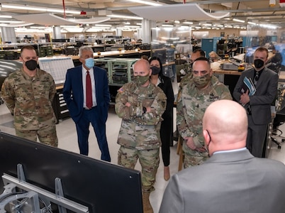 Photo of a group of people gather around a piece of military equipment to listen as a man gives a briefing.