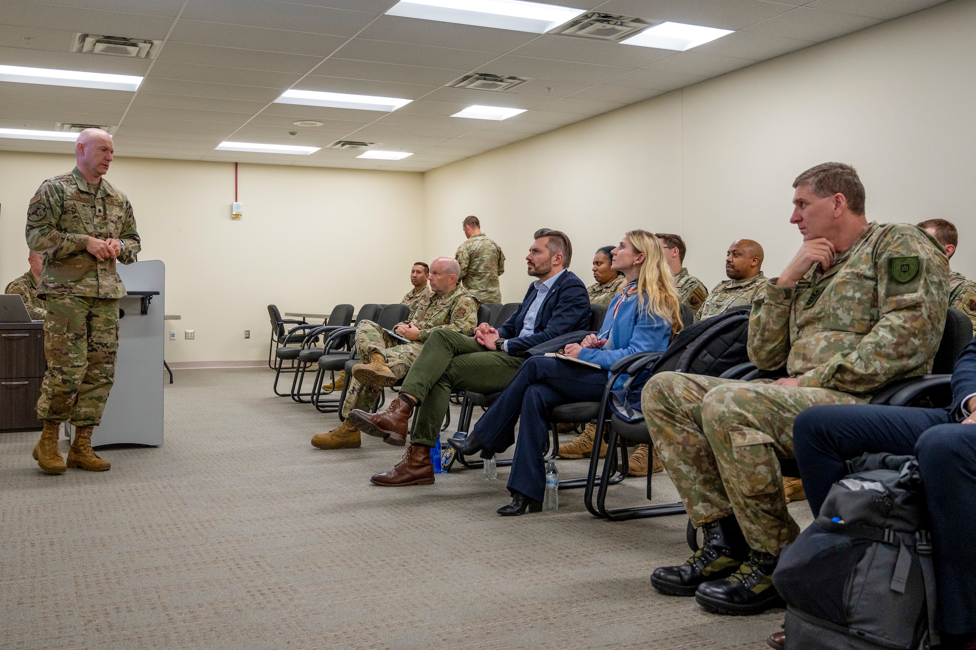 A man in U.S. Air Force Uniform briefs a room of people.