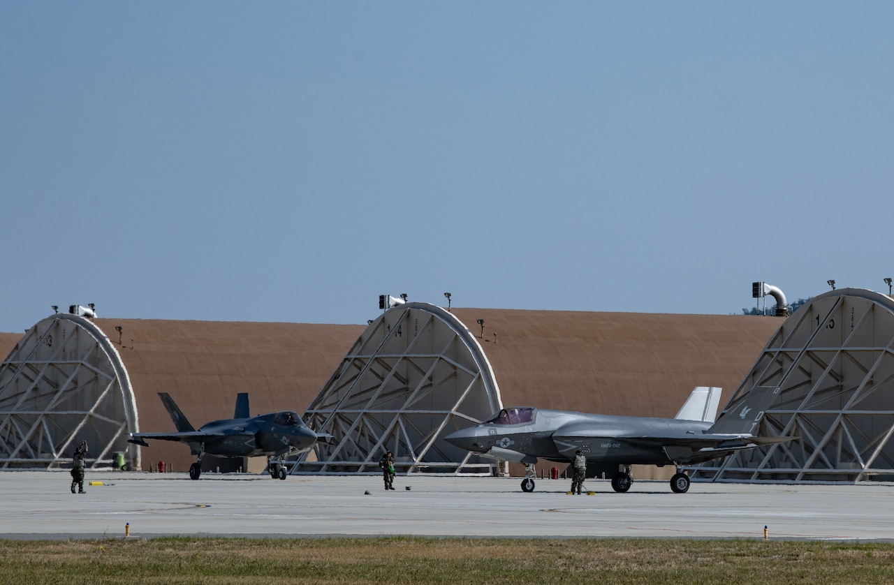 Two fighter jets are parked facing one another.