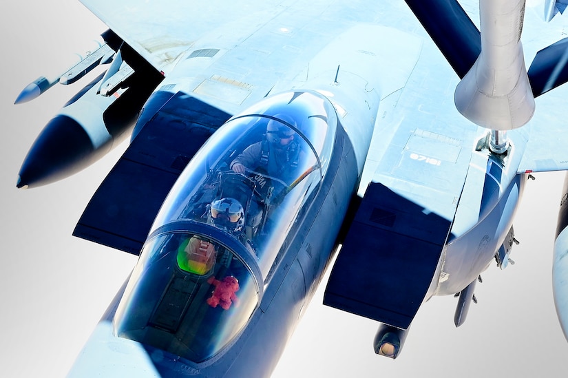 Two pilots are in the cockpit of a combat aircraft while it is being refueled in the air.