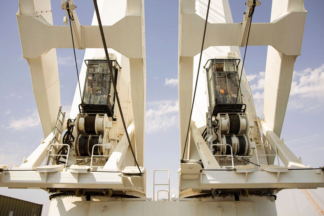 Two service members operate cranes next to each other.