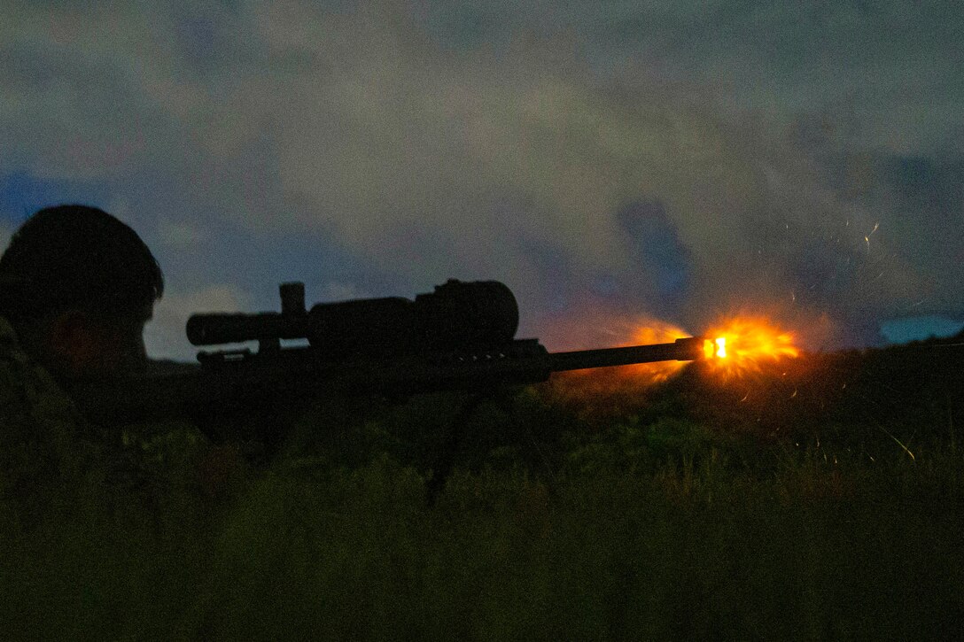 A Marine fires a weapon in the dark illuminated by orange ammo.