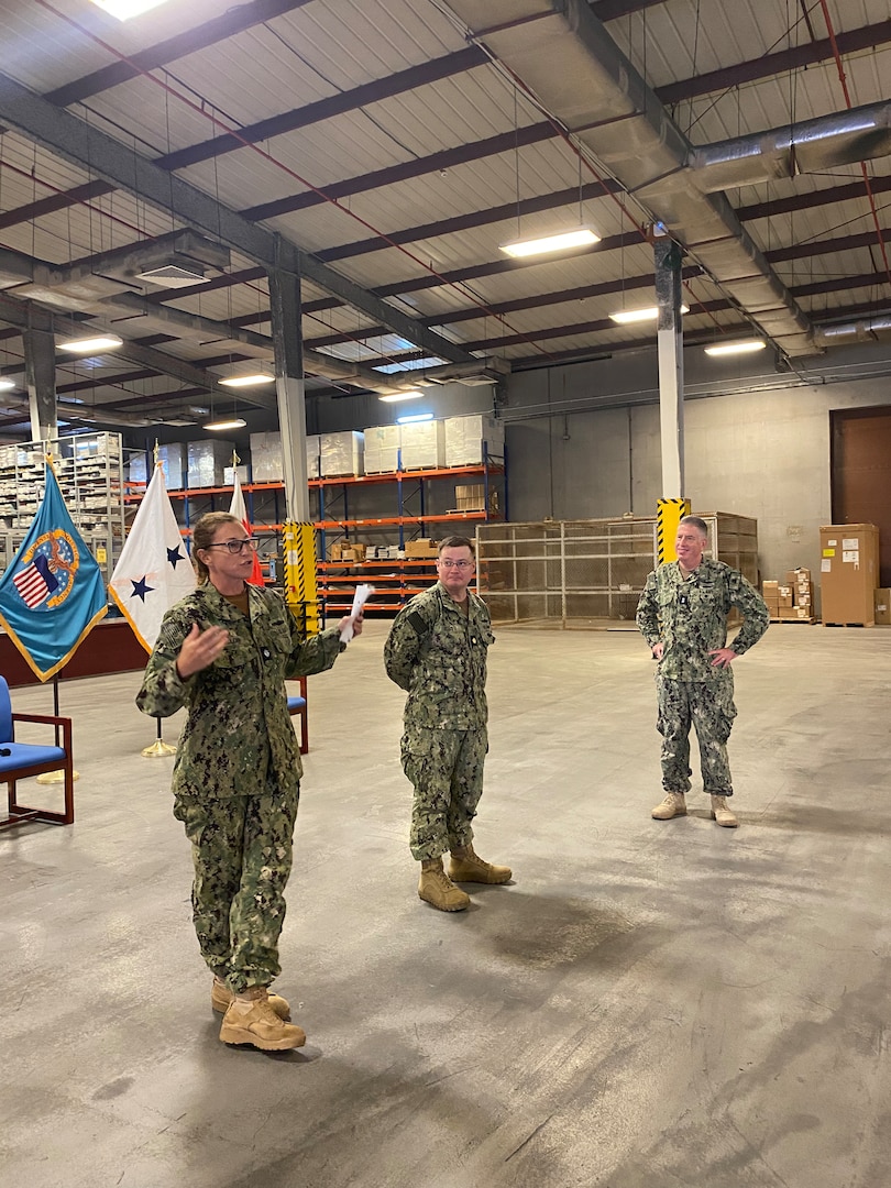 Three service members wearing camo stand apart from each other in a warehouse.