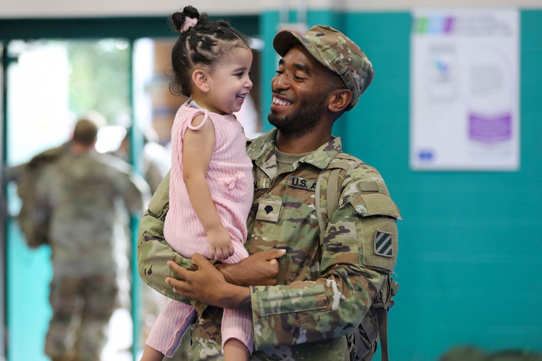 A soldier smiles as he holds his daughter.