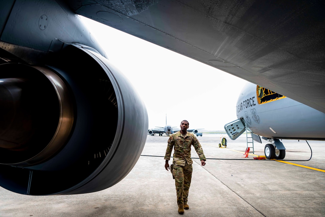 An airman walks under the wing of a parked aircraft.