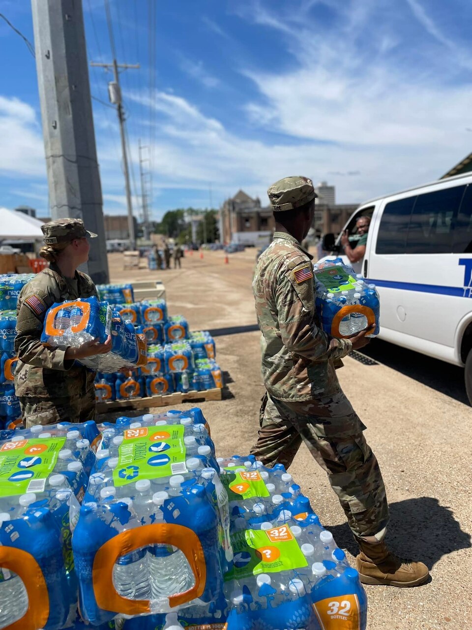 Two soldiers carrying cases of water speak to a resident in a vehicle.