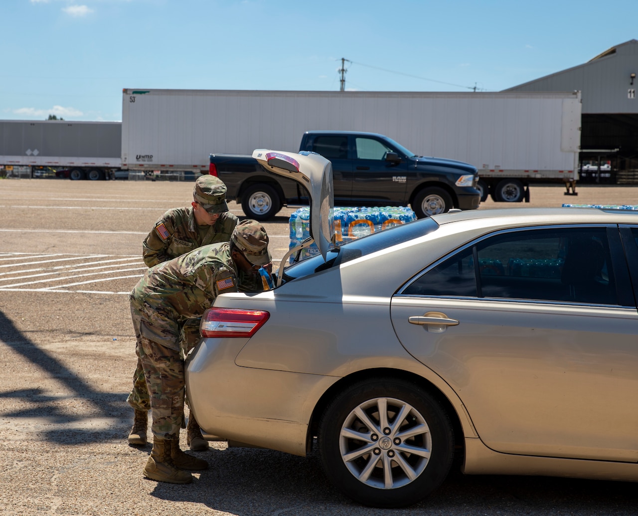 Two soldiers place water in the trunk of a car.