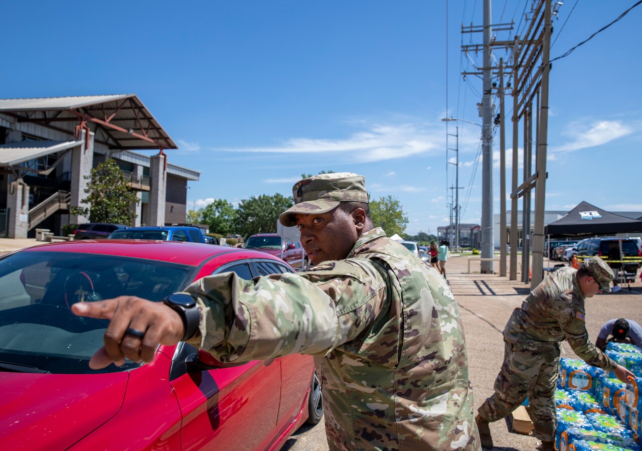 A soldier points out directions to the driver of a car.