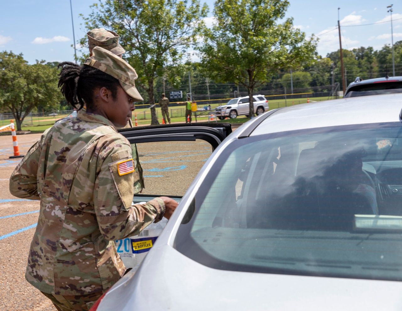 A soldier places a case of water on the back seat of a car.